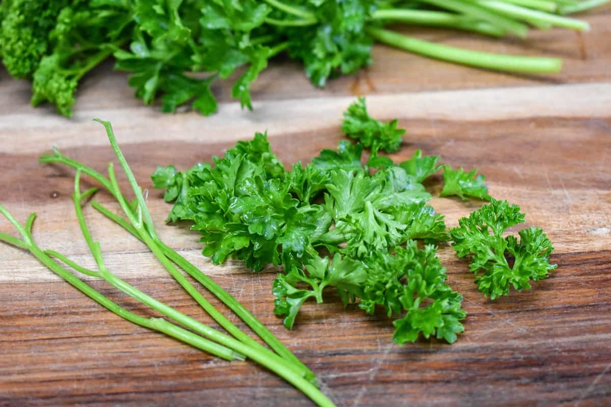 A few sprigs of parsley with the stems removed and separated from the leaves displayed on a wood cutting board.