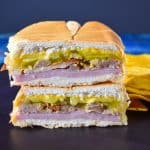 A close up image of the cuban sandwich displayed on a black surface with yellow plantain chips on the right hand side.