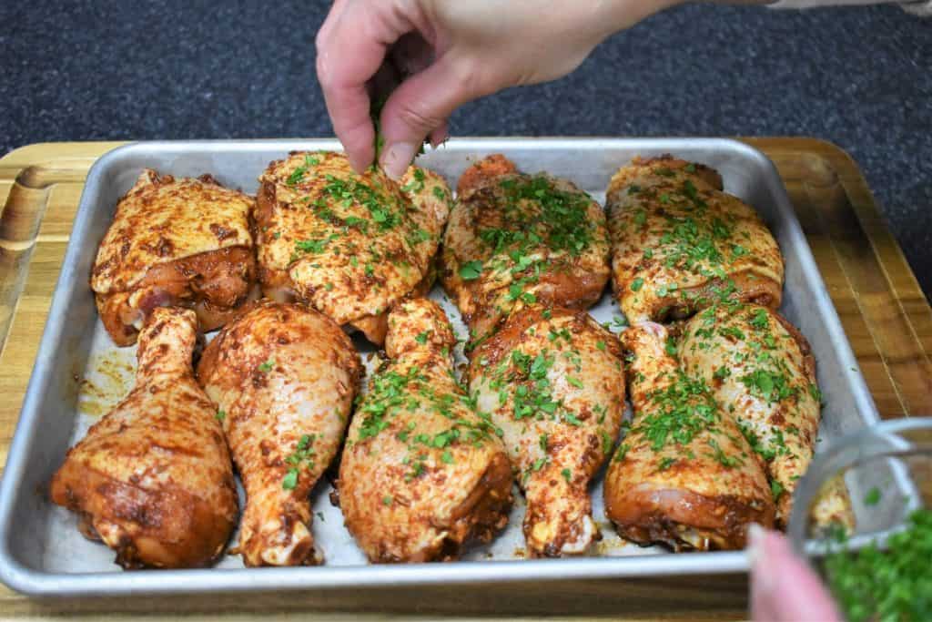 Seasoned Spicy Baked Chicken on a baking sheet being sprinkled with chopped parsley.