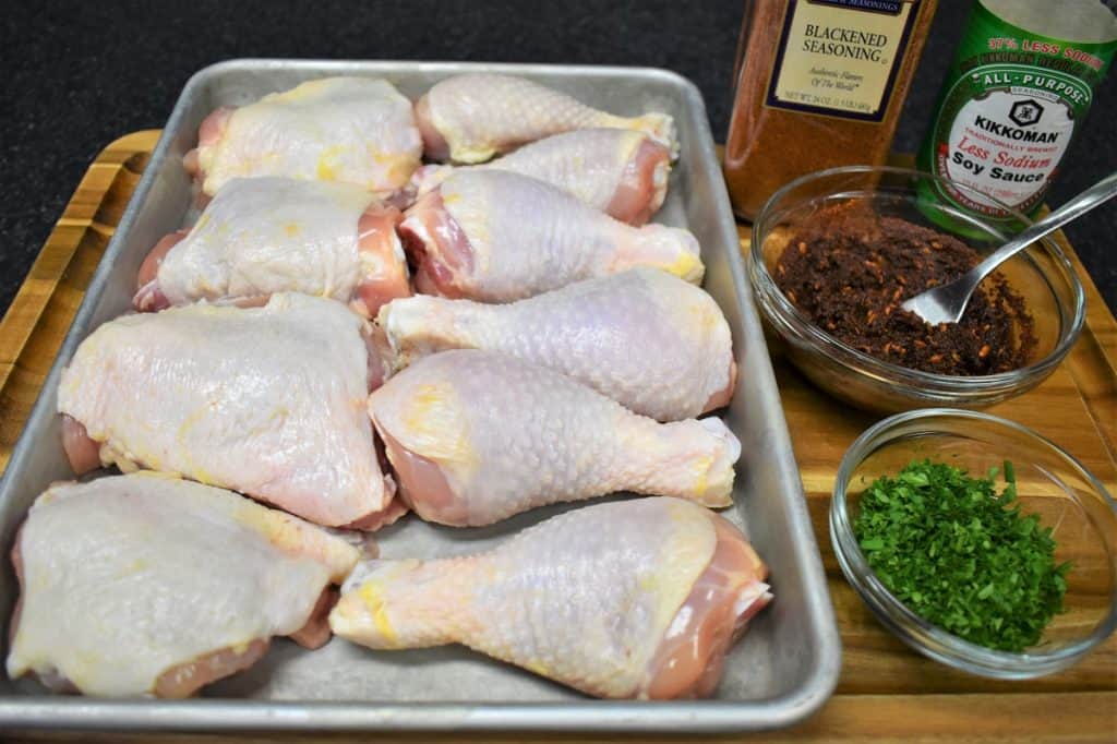 Spicy Baked Chicken Ingredients, the chicken, blackened seasoning paste and chopped parsley arranged on a wood cutting board