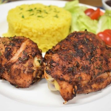 Spicy Baked Chicken, thigh and drum on a white plate with a side salad and yellow rice