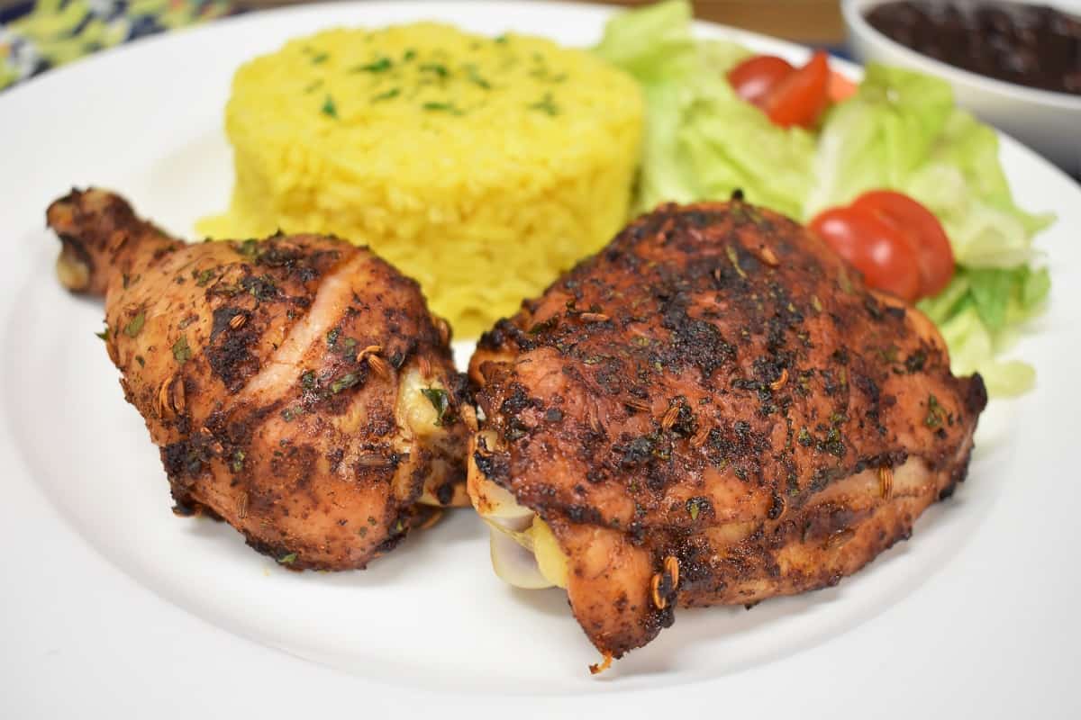 Spicy Baked Chicken, thigh and drum on a white plate with a side salad and yellow rice