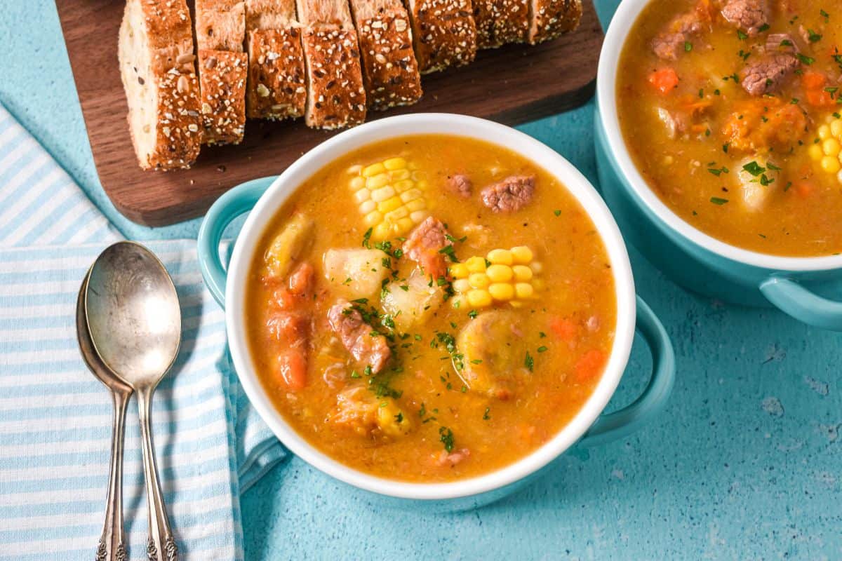 A top-down view of soup with corn and chunks of meat and vegetables, served alongside a napkin and spoons.