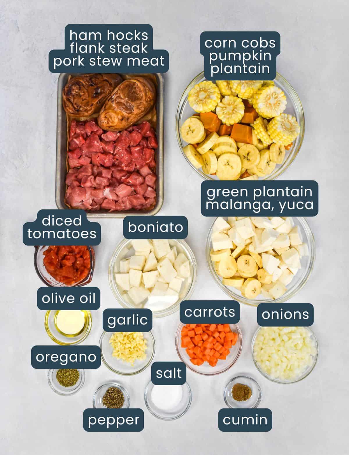 Ingredients for Cuban-style soup displayed in bowls and trays, including meat, root vegetables, plantains, tomatoes, spices, and oil.