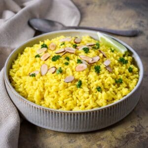 Easy yellow rice topped with toasted sliced almonds and fresh parsley in a serving bowl.