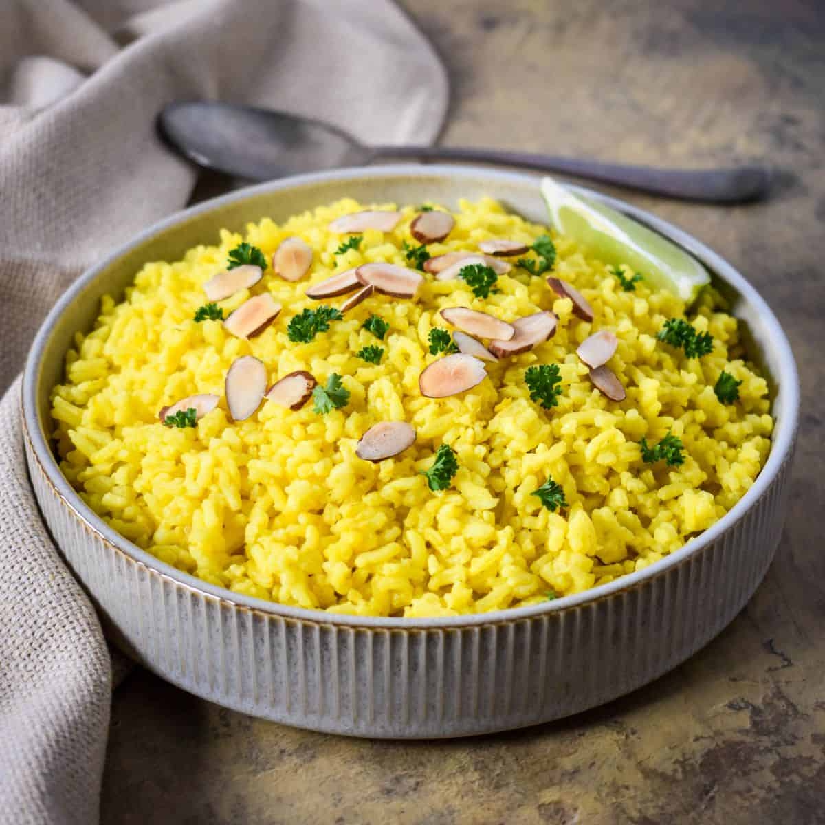 Easy yellow rice topped with toasted sliced almonds and fresh parsley in a serving bowl.