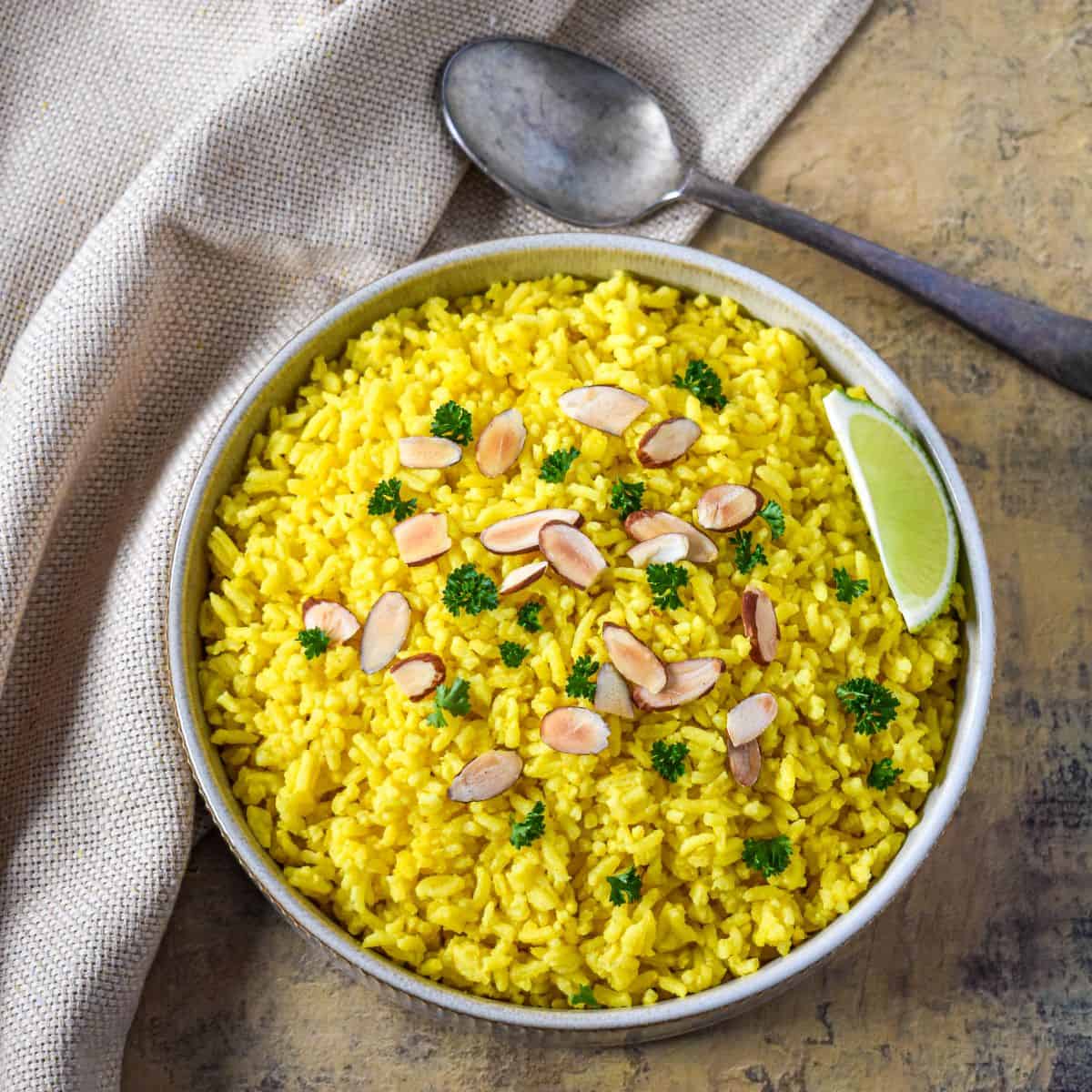 Overhead view of homemade yellow rice garnished with toasted almonds, parsley, and a lime wedge.
