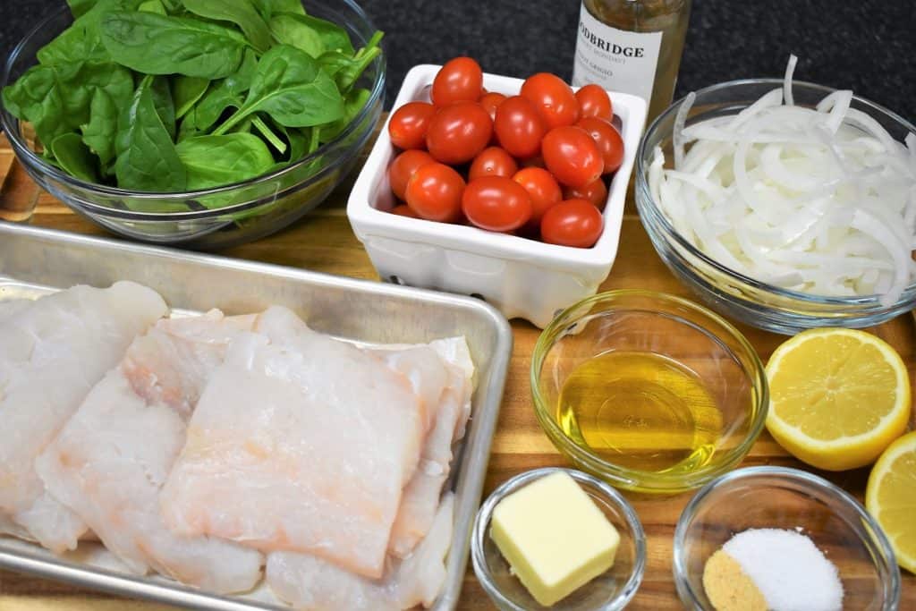 The ingredients for the cod with tomatoes dish displayed on a wood cutting board.