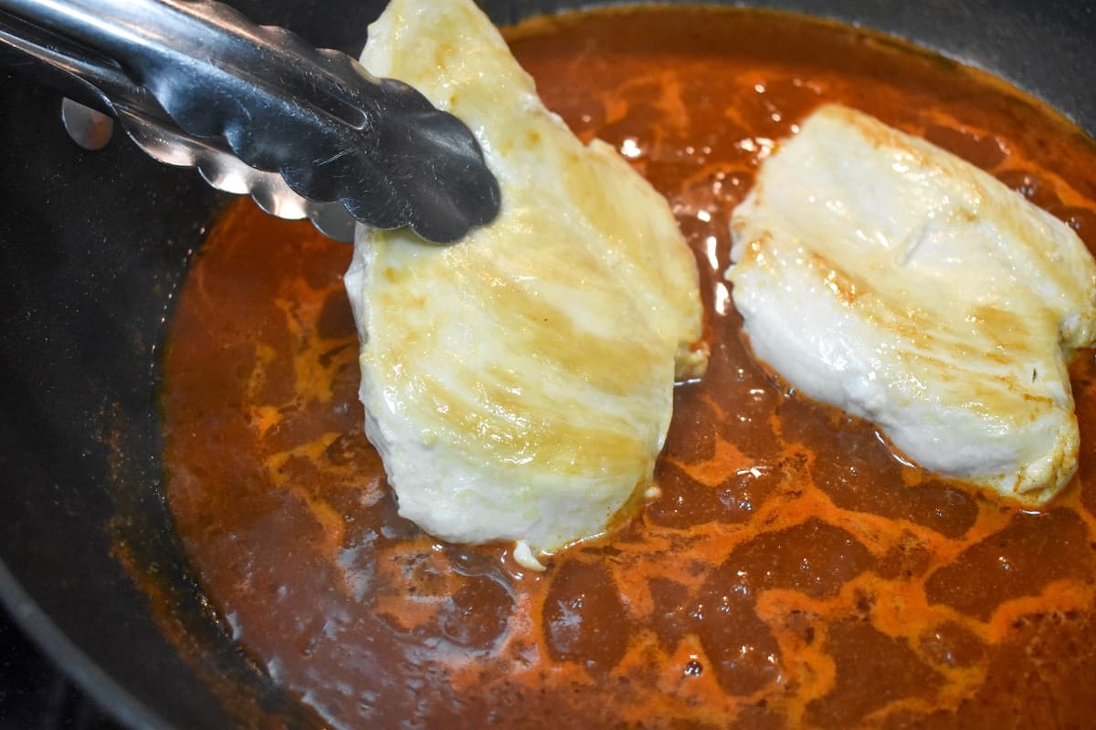 A browned chicken breast being added to a skillet with taco sauce.