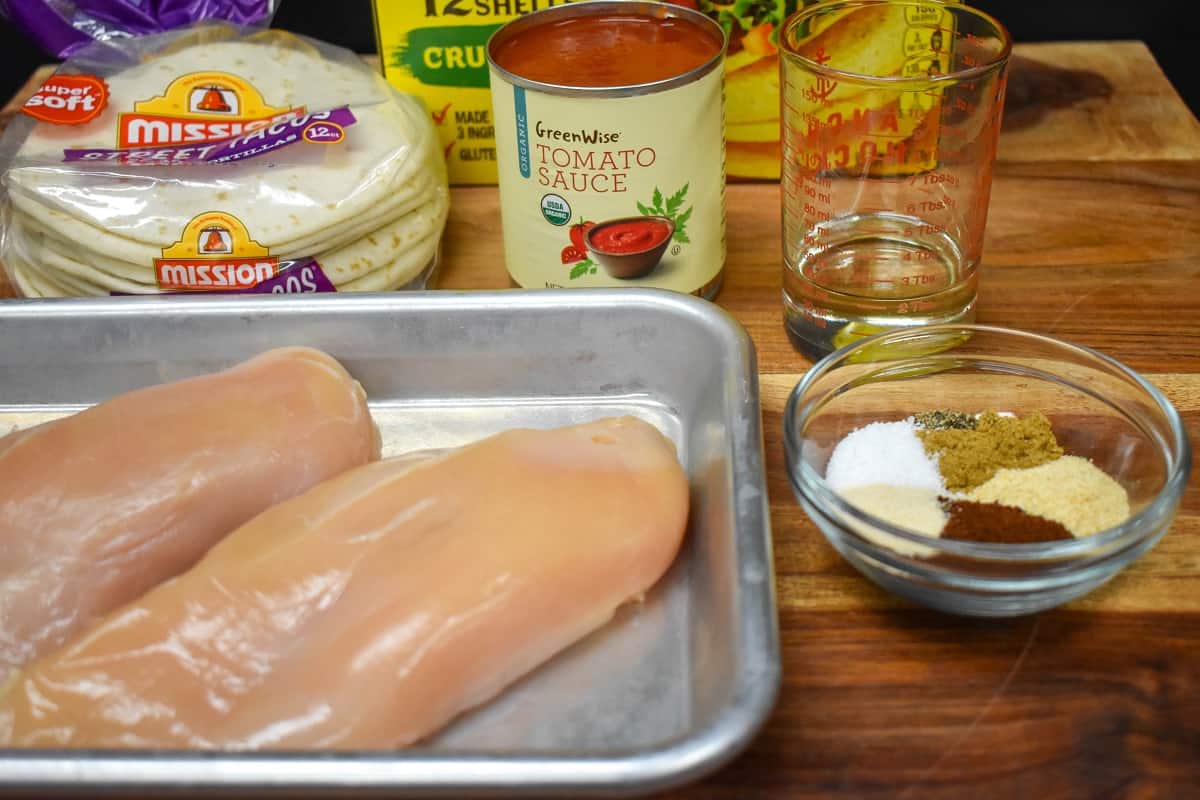 The ingredients for the shredded chicken tacos arranged on a wood cutting board.