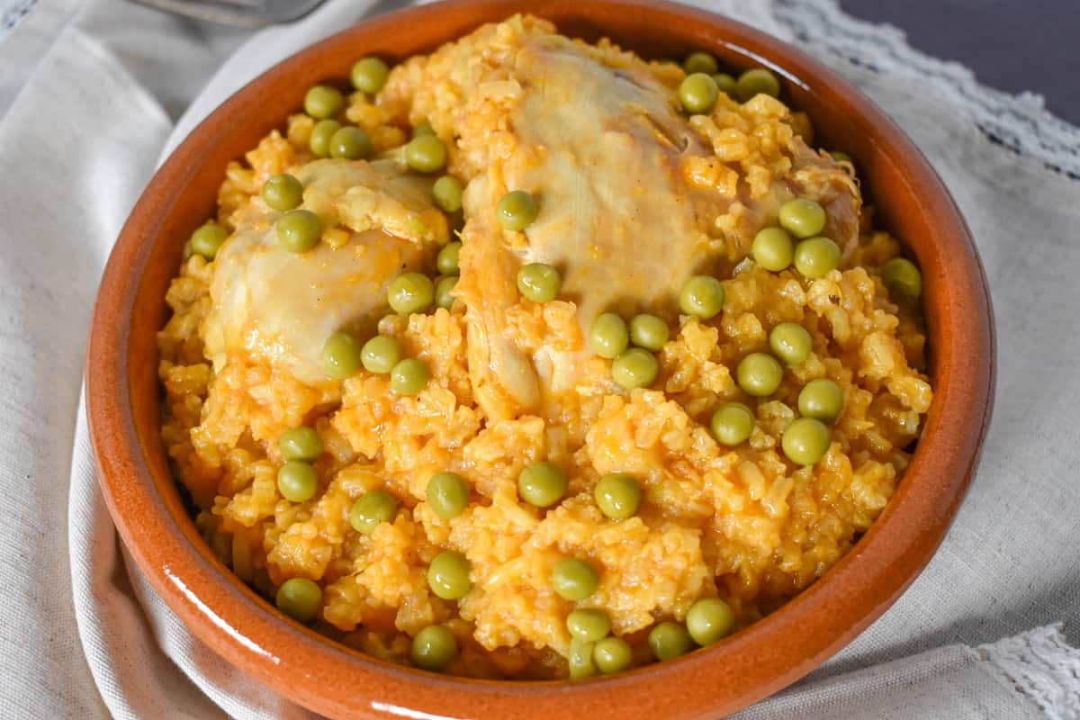 Arroz con pollo served in a terracotta bowl and garnished with sweet peas.