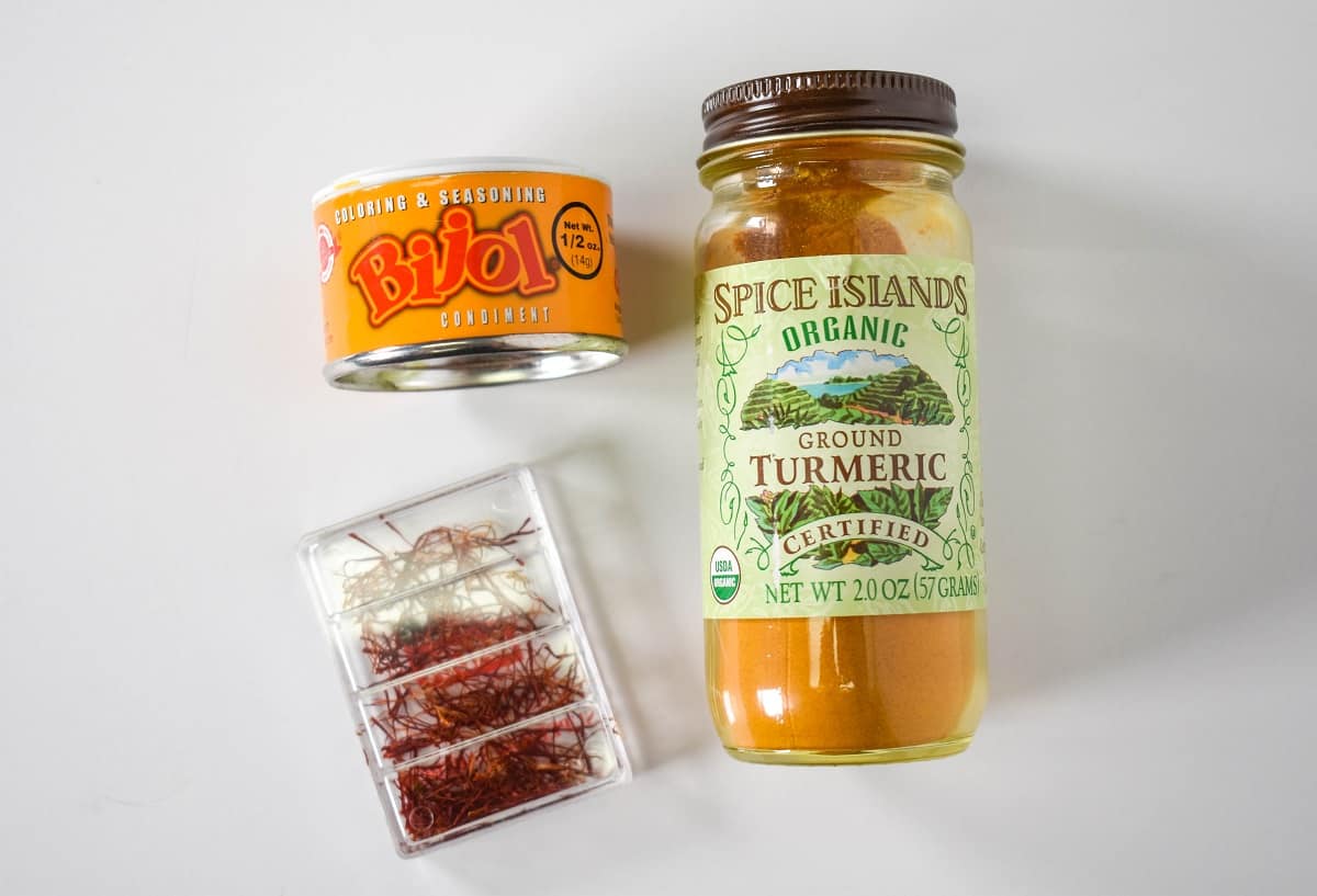 Saffron, turmeric and bijol displayed on a white table.