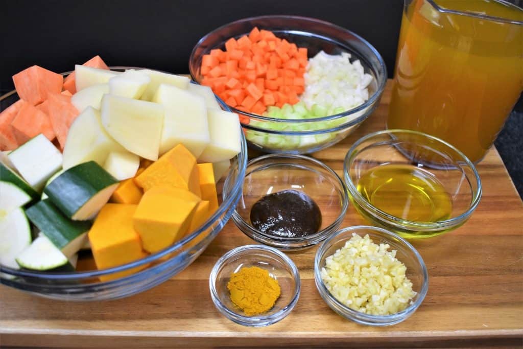 The ingredients for the creamy vegetable soup displayed on a wood cutting board.