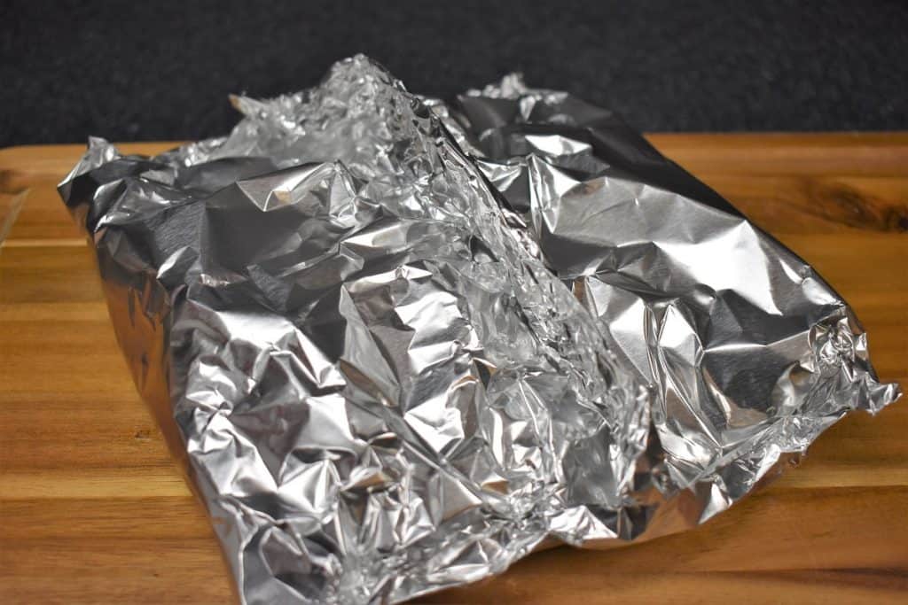 A sealed foil packet of potatoes set on a wood cutting board.