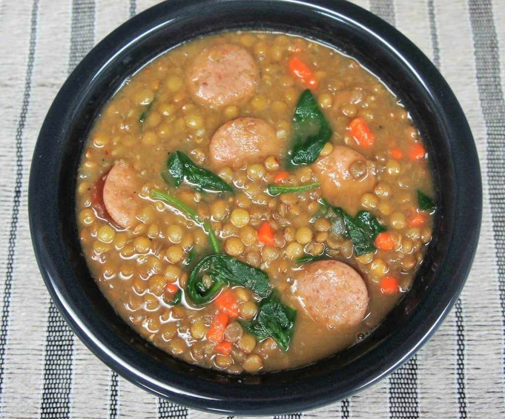 Lentil sausage soup served in a dark gray bowl.