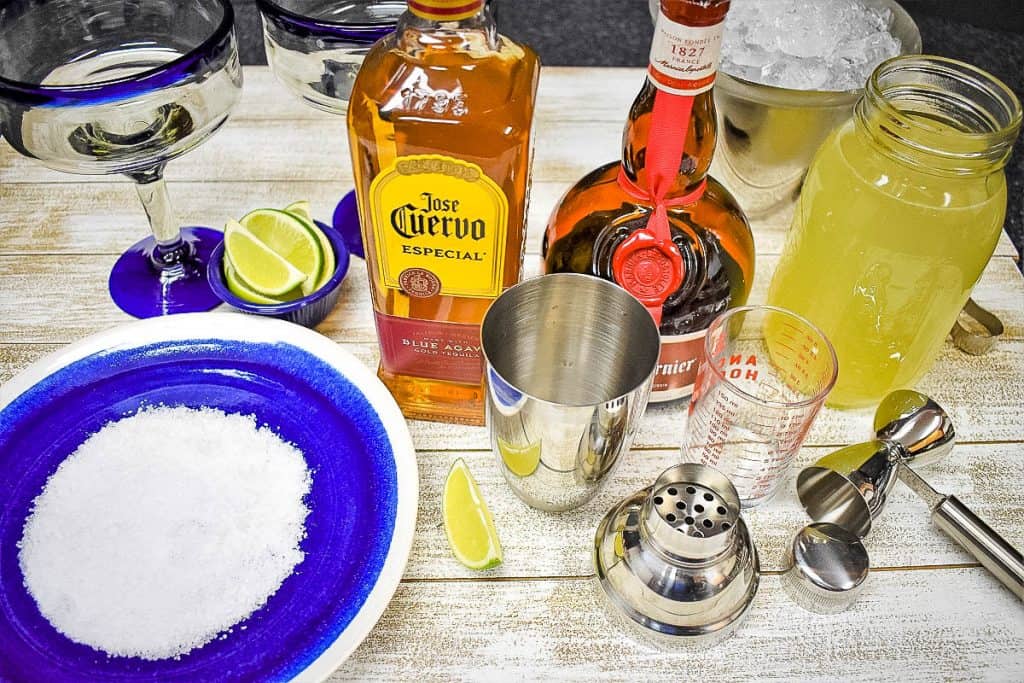 Ingredients for a homemade margarita displayed on a white wood board.