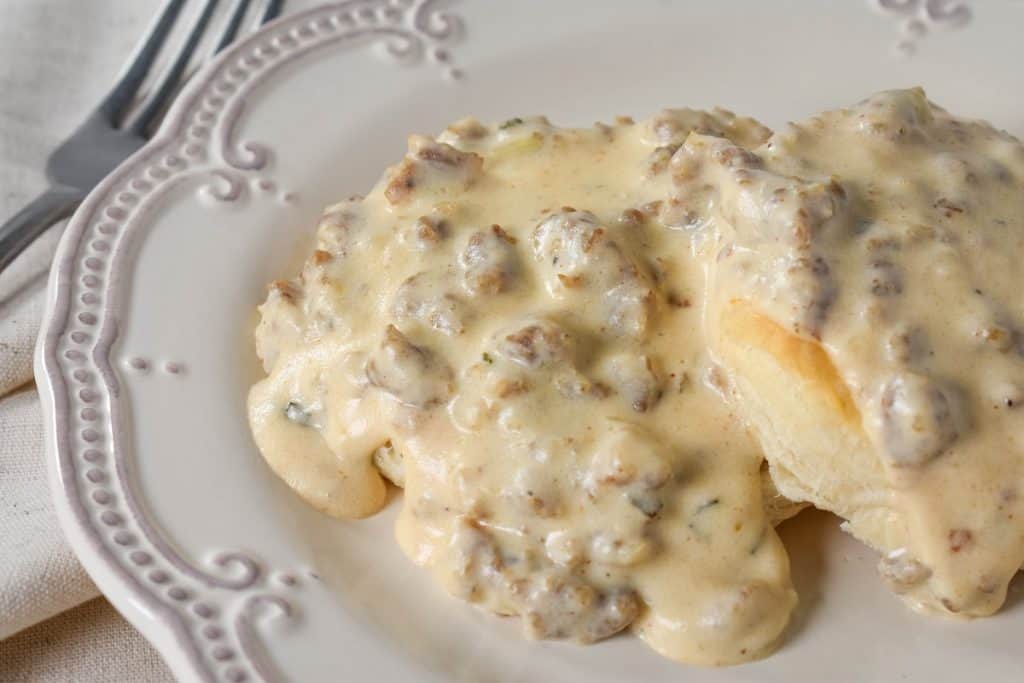A close up image of sausage gravy served over biscuits on a white plate.