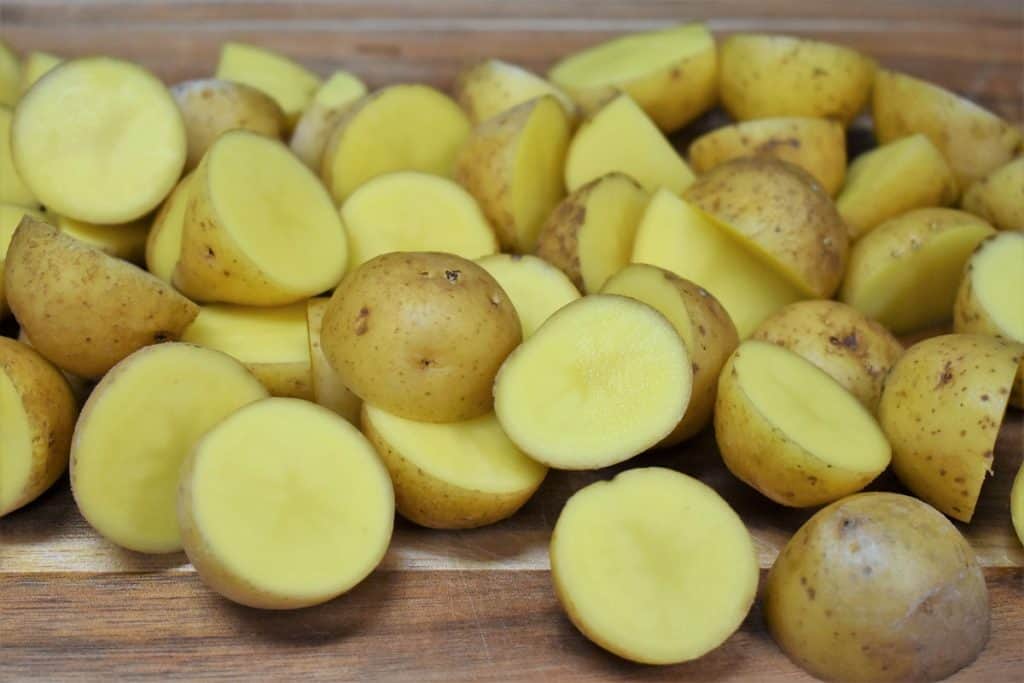 Raw, small honey gold potatoes cut in half displayed on a wood cutting board.