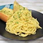 Spaghetti Aglio e Olio served on a black plate with two pieces of garlic toast in the background.