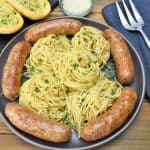 A large platter of spaghetti aglio e olio with Italain sausage arranged around the pasta.