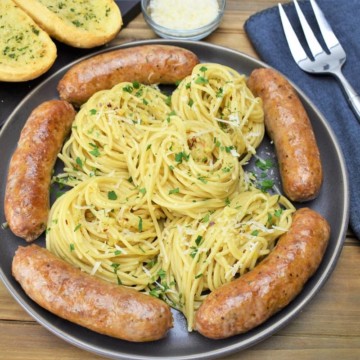 A large platter of spaghetti aglio e olio with Italain sausage arranged around the pasta.