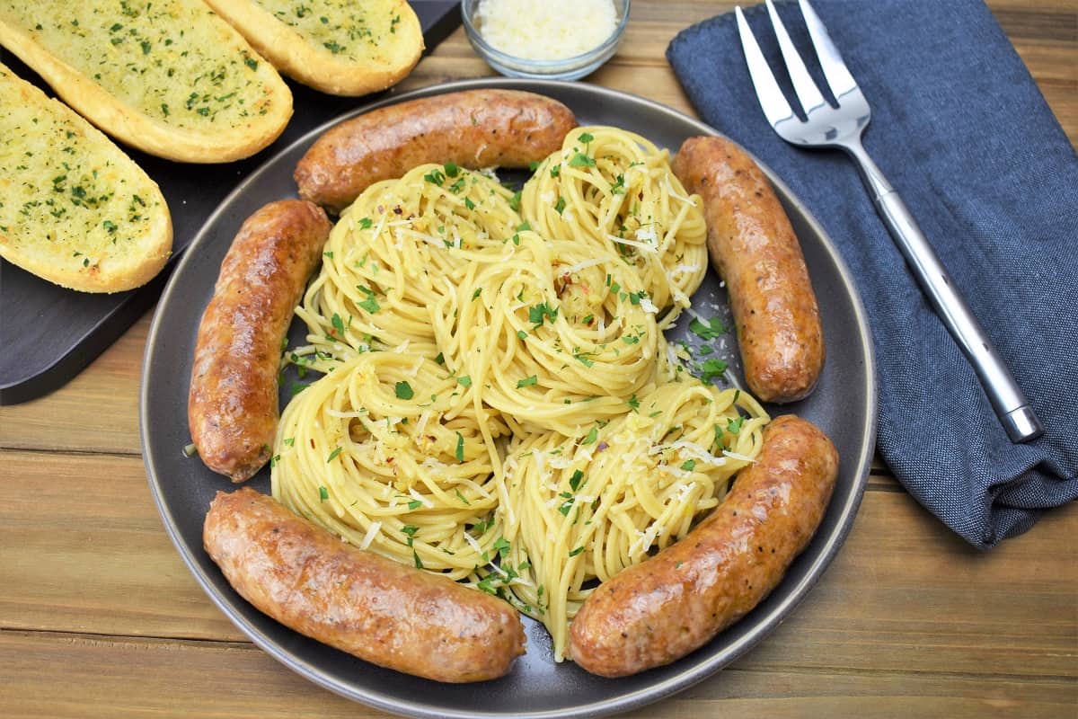A large platter of spaghetti aglio e olio with Italain sausage arranged around the pasta.