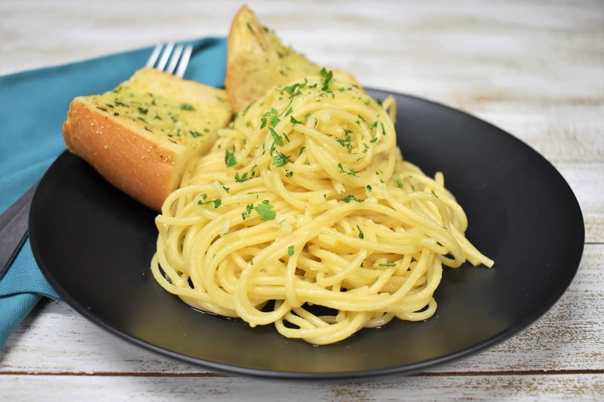 Spaghetti Aglio e Olio served on a black plate with two pieces of garlic toast in the background.