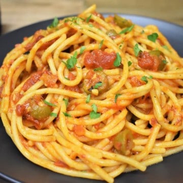 Spaghetti and a tomato olive sauce served on a black plate.