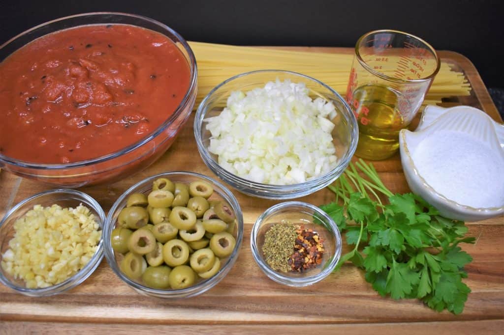 The ingredients of tomato and olive pasta displayed on a wood cutting board.