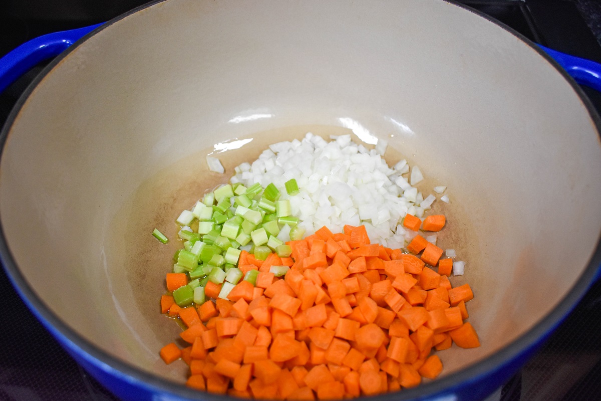Diced onions, carrots, and celery added to a large, white and blue pot.
