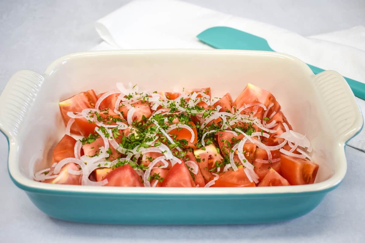 An image of the cut tomatoes with the onions and parsley in a shallow baking dish.