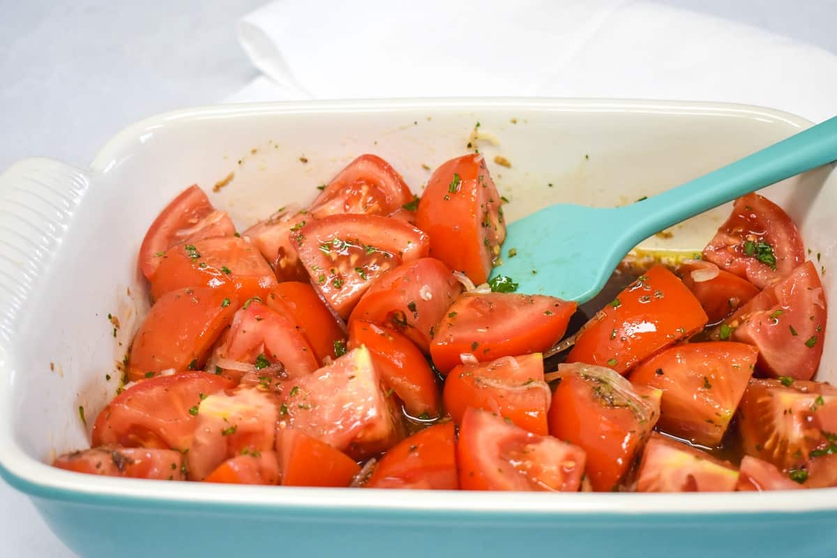 An image of the tomatoes being tossed with a light blue silicone spatula.