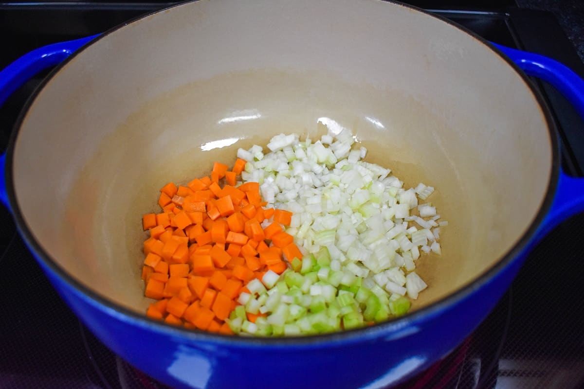 Diced onions, carrots, and celery cooking in a large, blue pot.