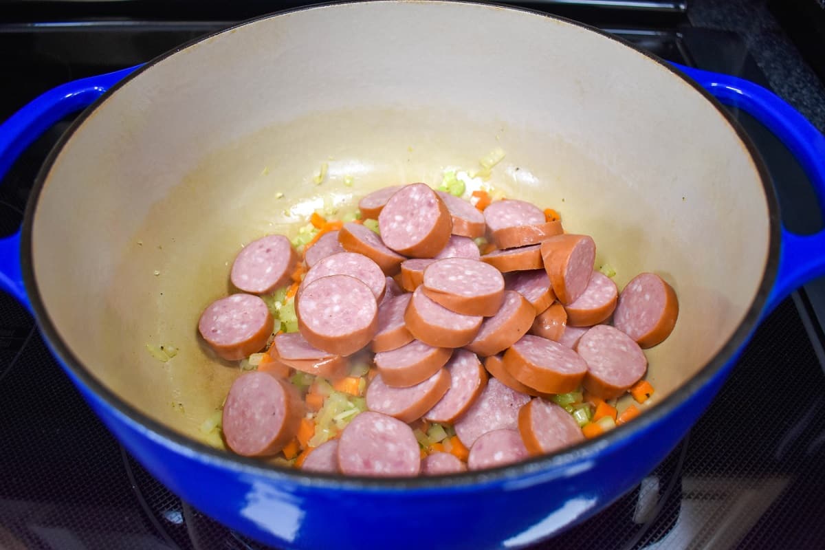 Sliced kielbasa sausage added to the ingredients in large pot.