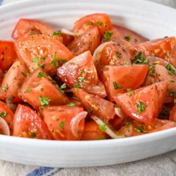A close-up image of the marinated tomatoes served in a white bowl.