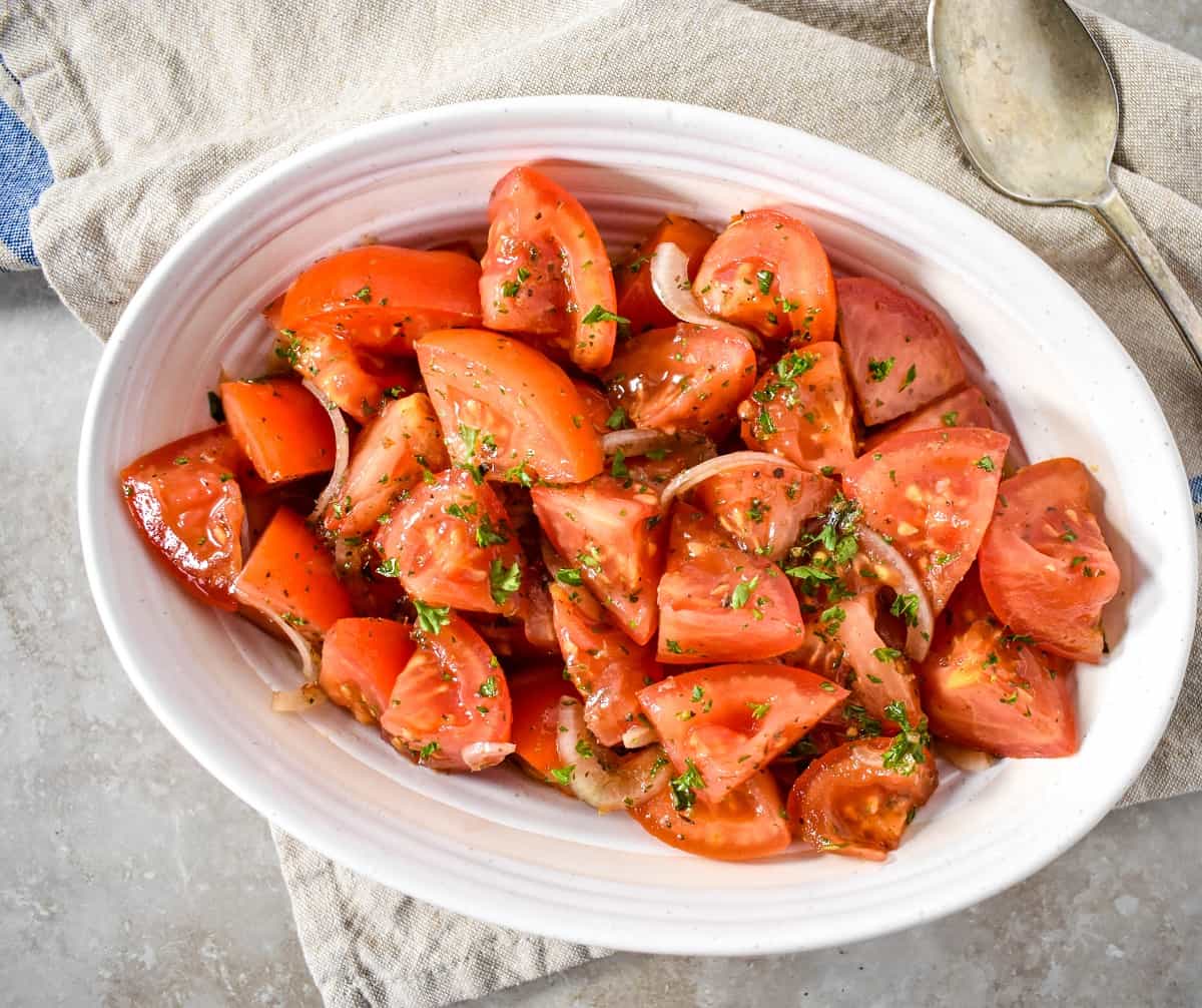 An image of the marinated tomatoes served in a white bowl with a beige linen.
