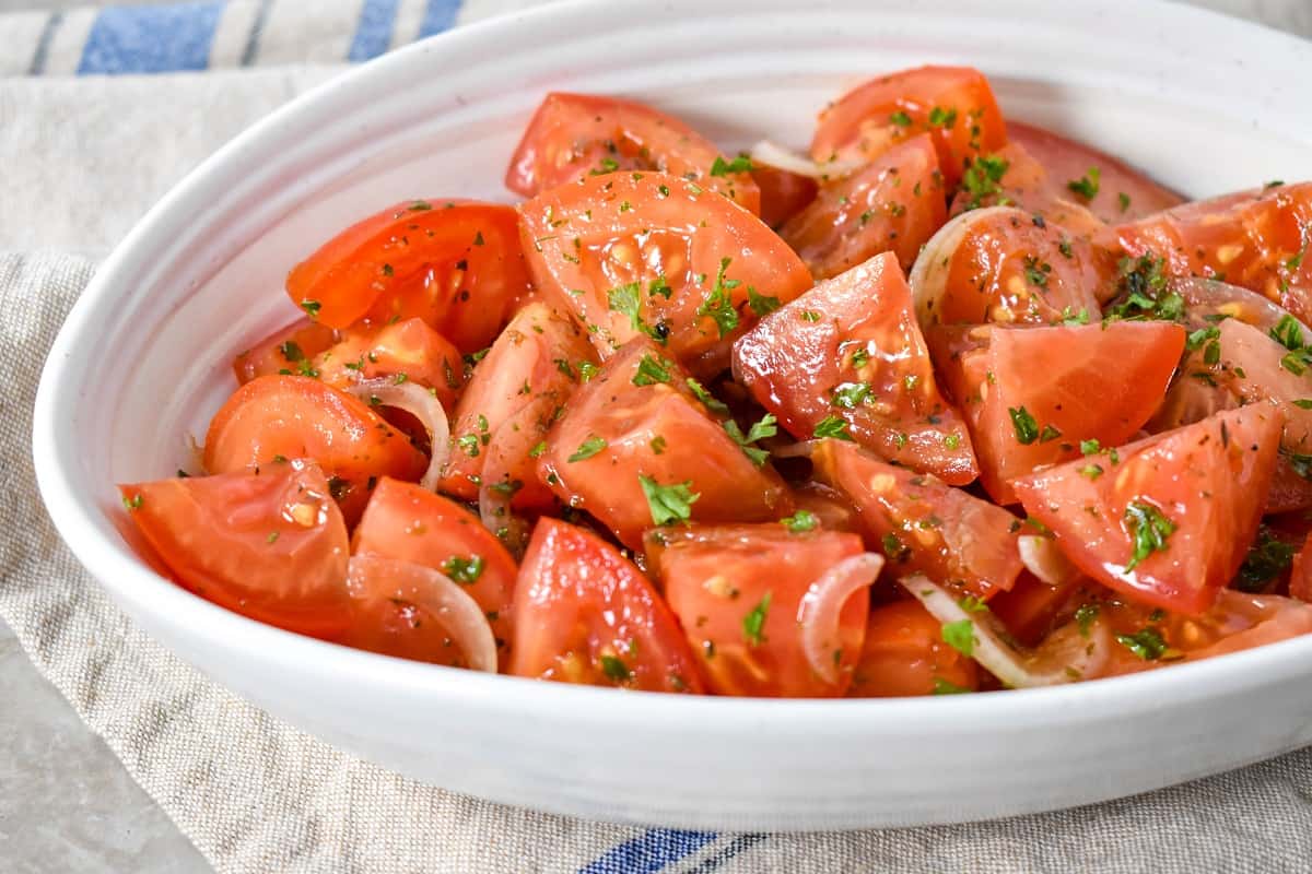 An image of the marinated tomatoes served in a white bowl with a beige linen.