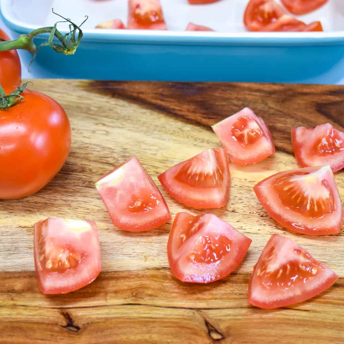 A tomato cut into pieces on a wood cutting board.