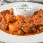 The beef and potatoes served in a white plate with white rice.