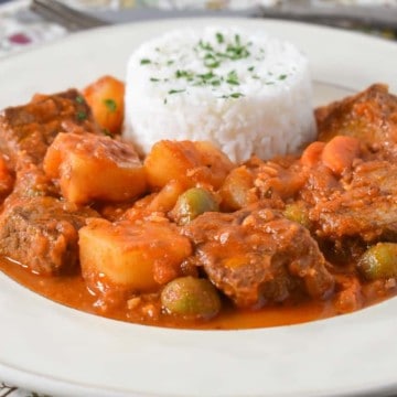 The beef and potatoes served in a white plate with white rice.