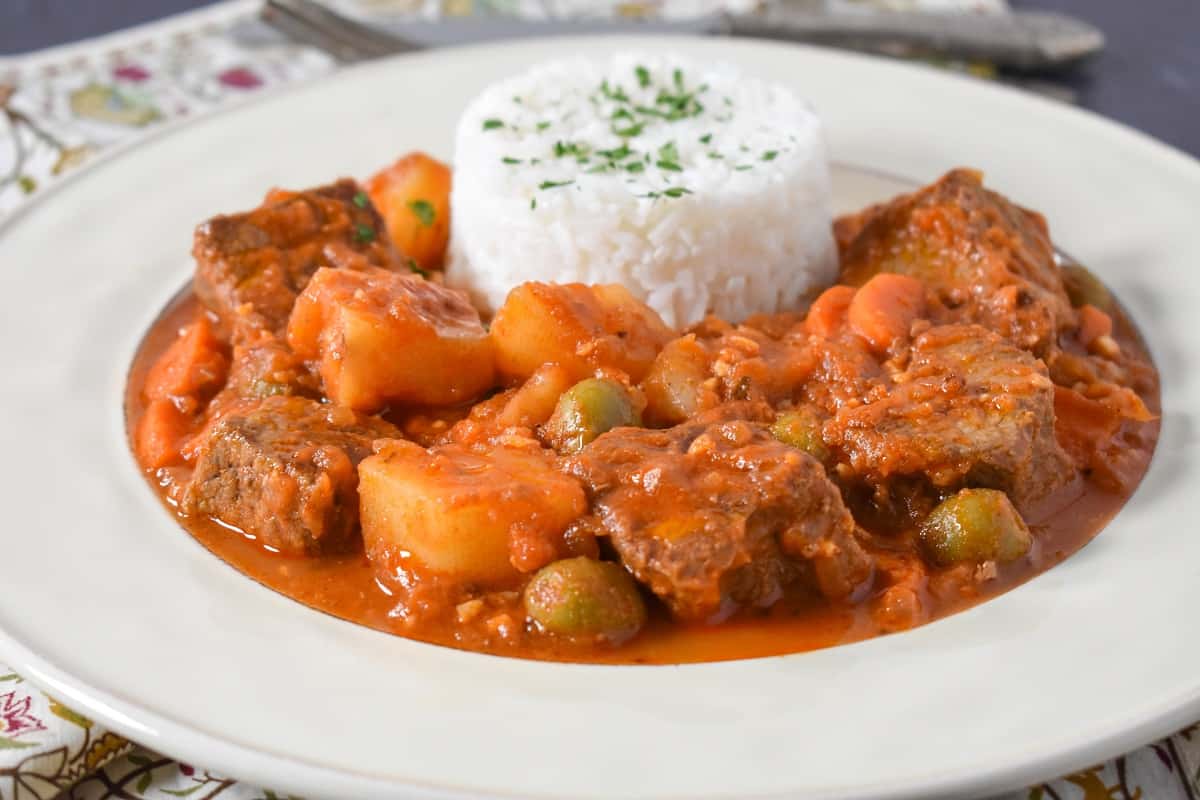 The beef and potatoes served in a white plate with white rice.