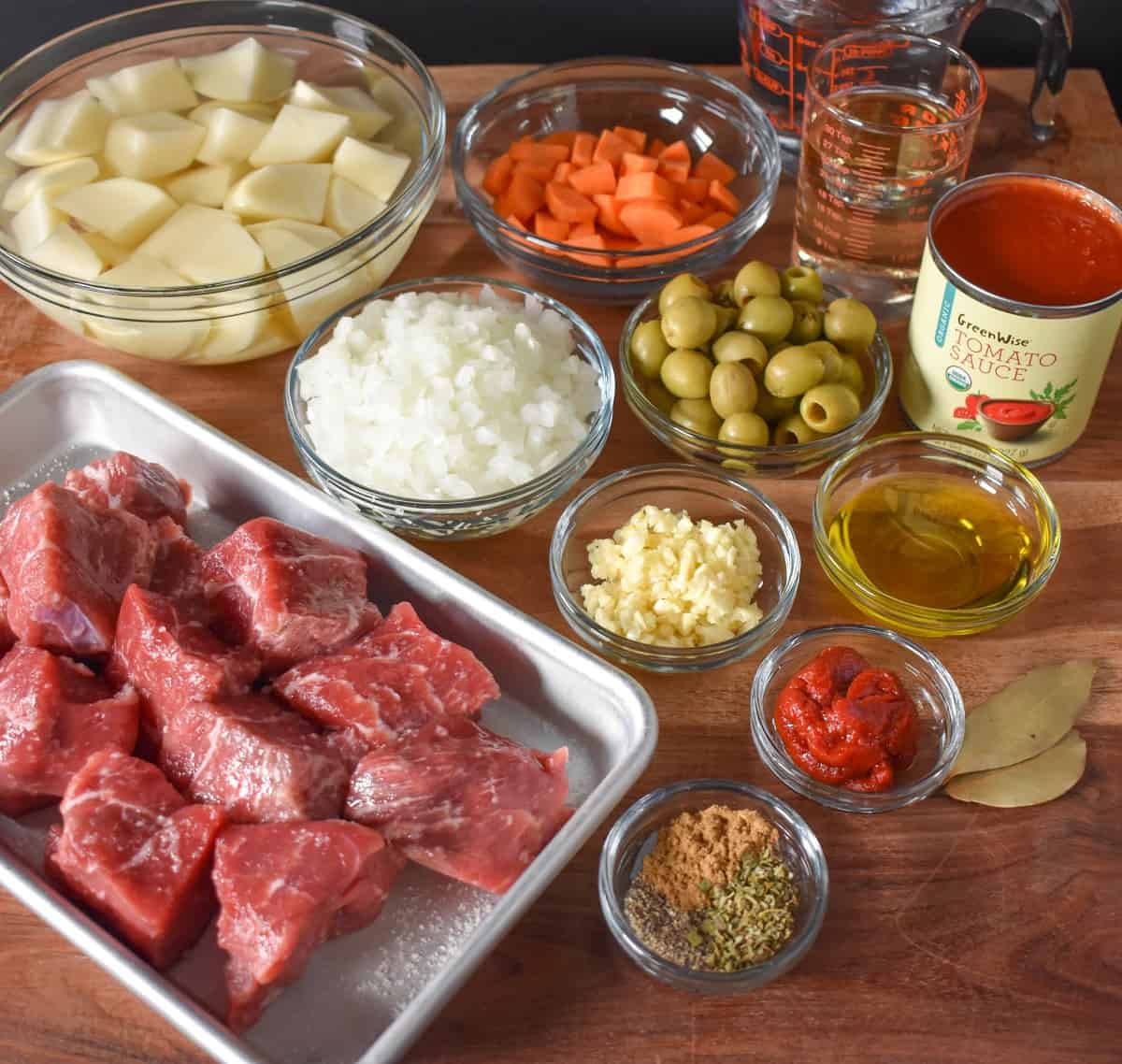 The prepped ingredients separated in glass bowls and a small sheet pan for the beef all arranged on a large wood cutting board.