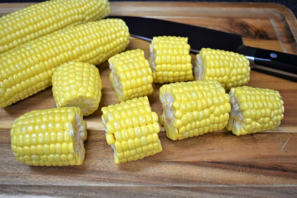 Fresh corn cobs cut into four pieces, displayed on a wood cutting board.