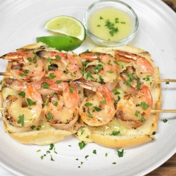 Two grilled shrimp skewers and butter lime sauce served on toasted bread on a white plate and garnished with parsley.