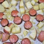 Baked sliced sausage and diced red potatoes arranged on a large baking sheet..