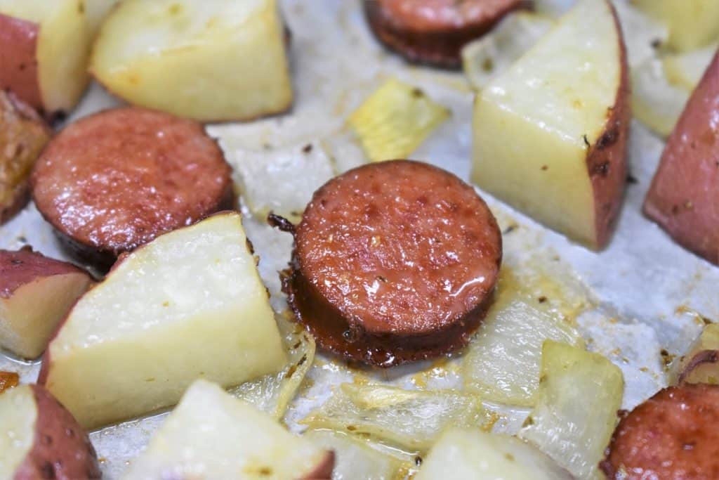 A close up image of a sausage rounds and diced red tomatoes on a metal baking sheet.