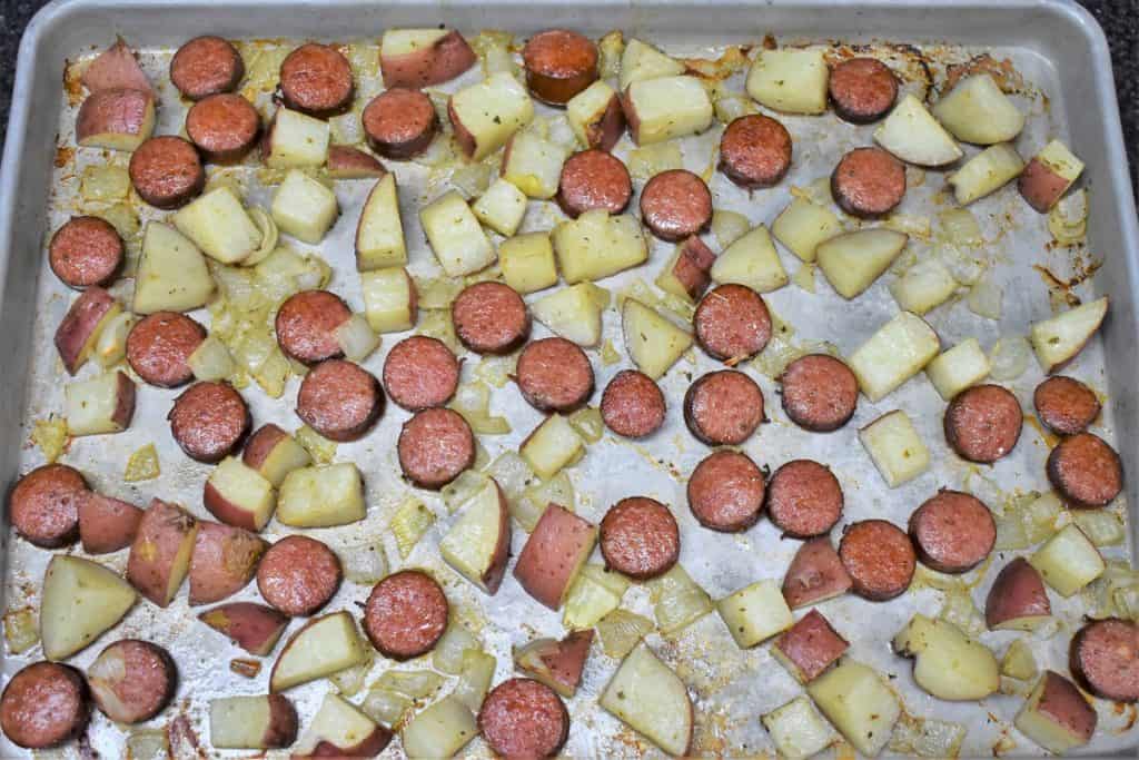 Baked sliced sausage and diced red potatoes arranged on a large baking sheet.