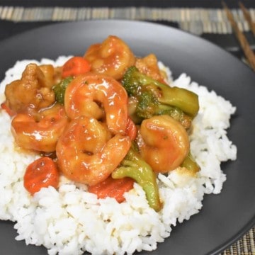 Shrimp and mixed vegetable stir fry served on a bed of white rice on a black plate.