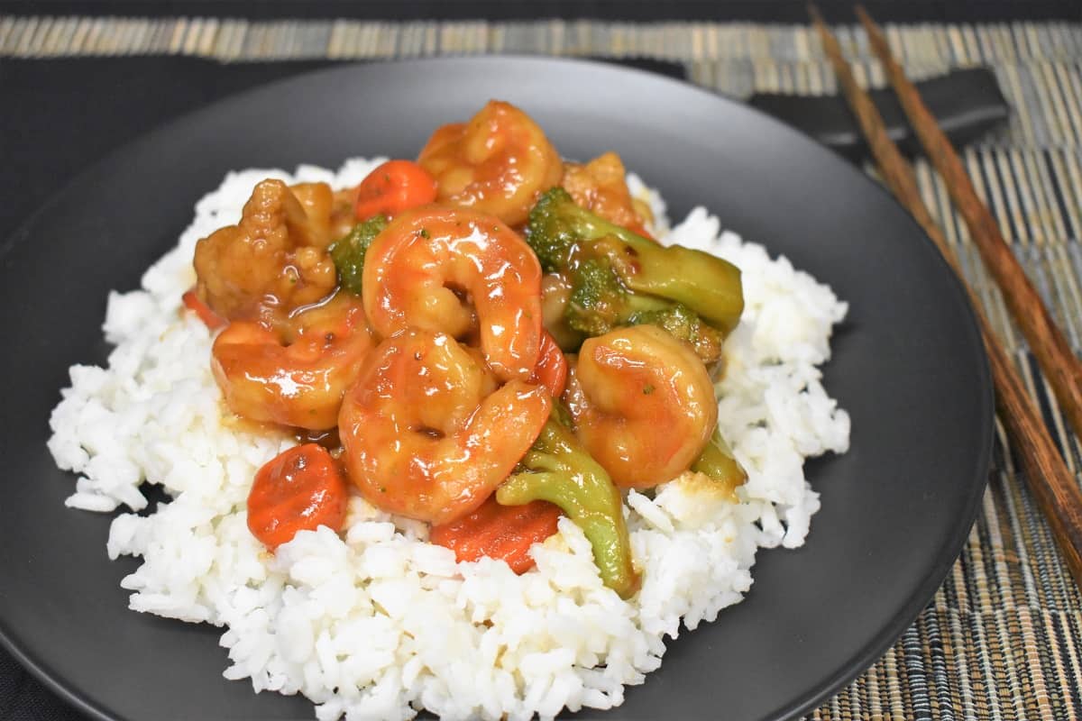 Shrimp and mixed vegetable stir fry served on a bed of white rice on a black plate.