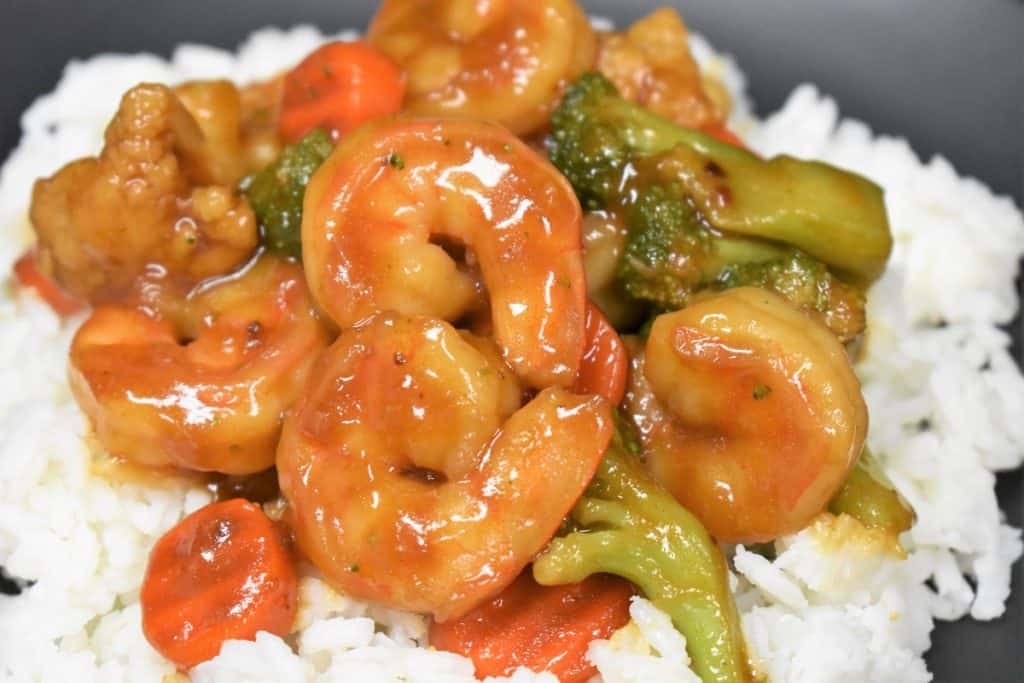 A close up image of shrimp and vegetable stir fry on a bed of white rice.